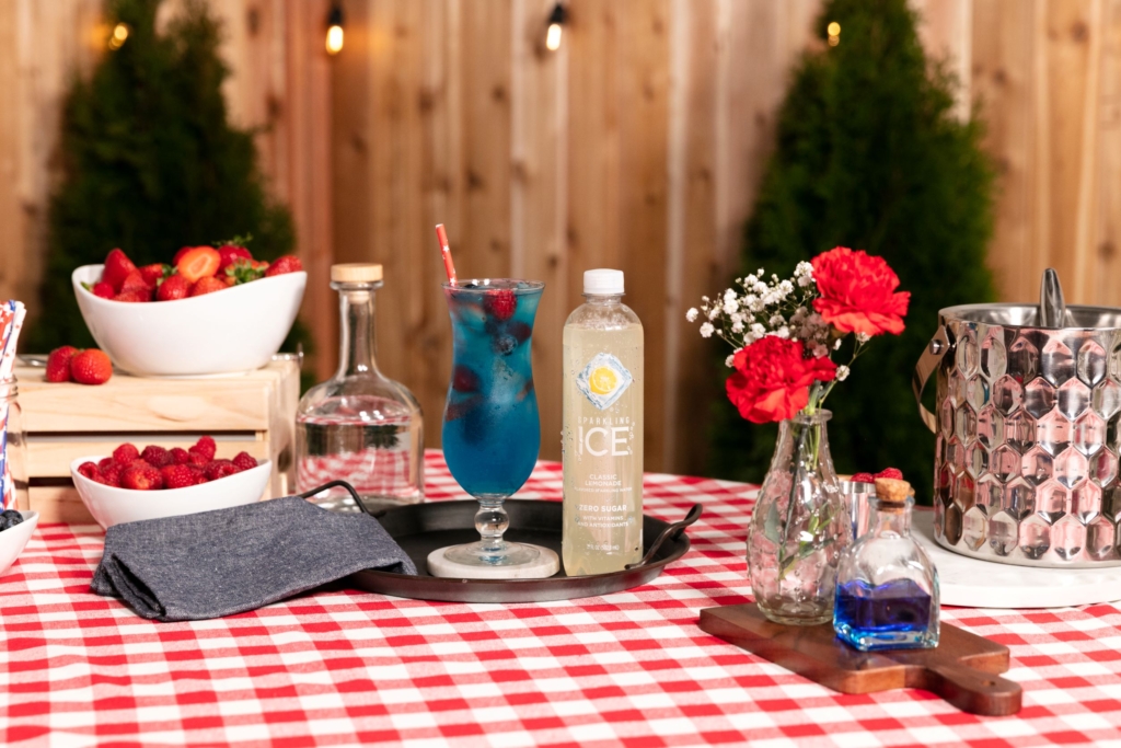 Sparkling Ice America the Blue Cocktail on a table next to fresh flowers.