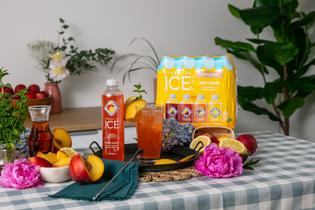 Sparkling Ice Sunshine Peach Tea mocktail on table with Sparkling Ice Lemonade Variety 12 Pack and fresh peaches.